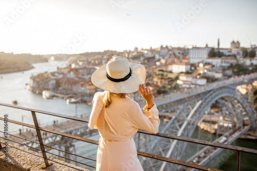 Young woman tourist enjoying beautiful aerial cityscape view with famous bridge during the sunset in Porto city, Portugal