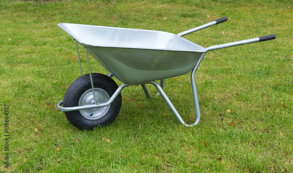 Wheelbarrow on a green grass field. Garden metal wheelbarrow cart. Wheelbarrow on a green grass field. Garden metal wheelbarrow cart.
