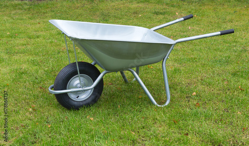 Wheelbarrow on a green grass field. Garden metal wheelbarrow cart.