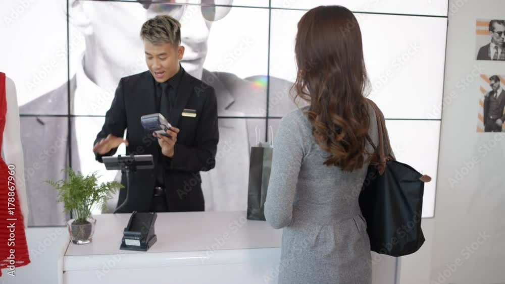 Group of women shopping in clothing store, one woman makes contactless payment with smartphone.