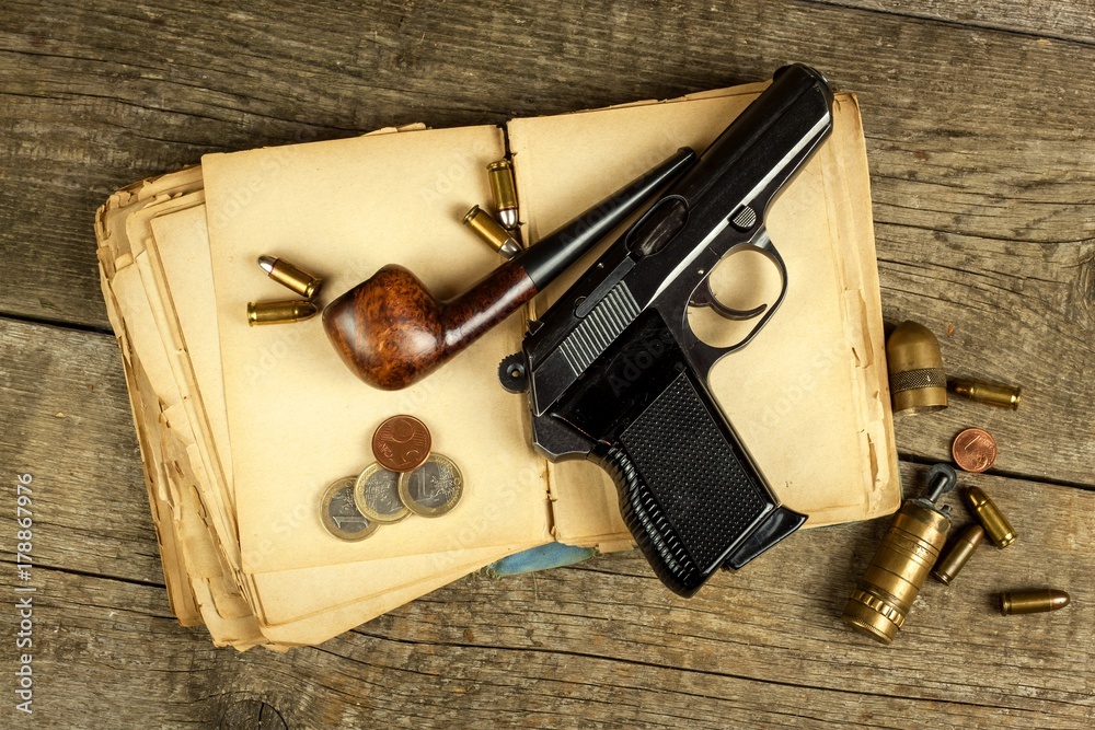 Gun and old book. Detective novel. Wooden tobacco pipe. Pistols and cartridges on the table.