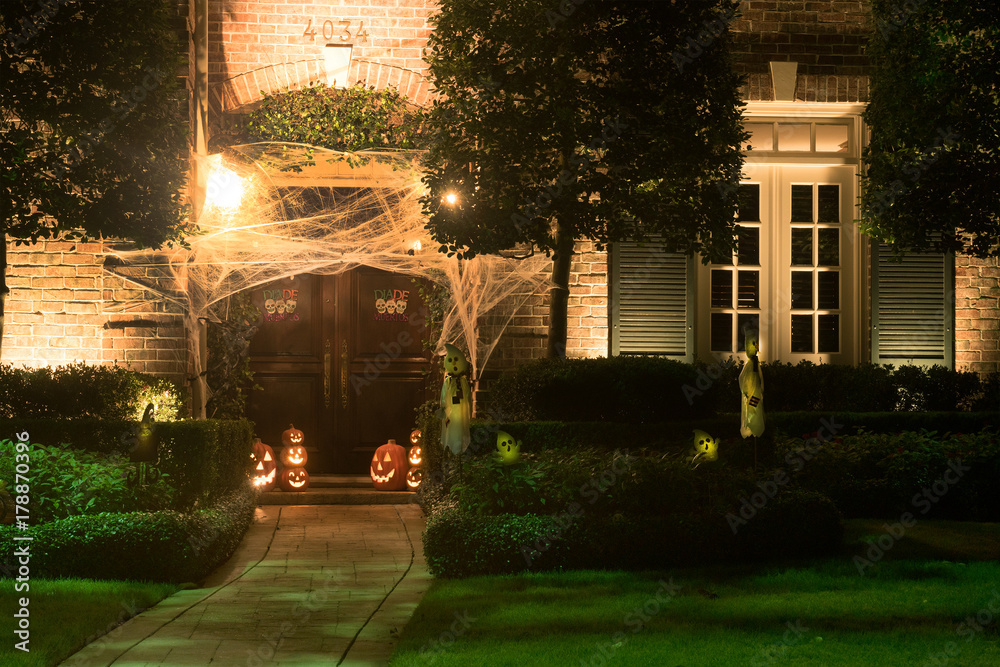 Naklejka premium The house is decorated for Halloween: the entrance to the house is tightened with cobwebs, pumpkins with carved mugs and glowing from within. Night