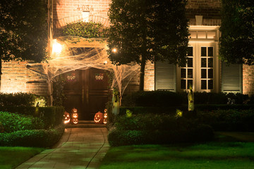 The house is decorated for Halloween: the entrance to the house is tightened with cobwebs, pumpkins with carved mugs and glowing from within. Night
