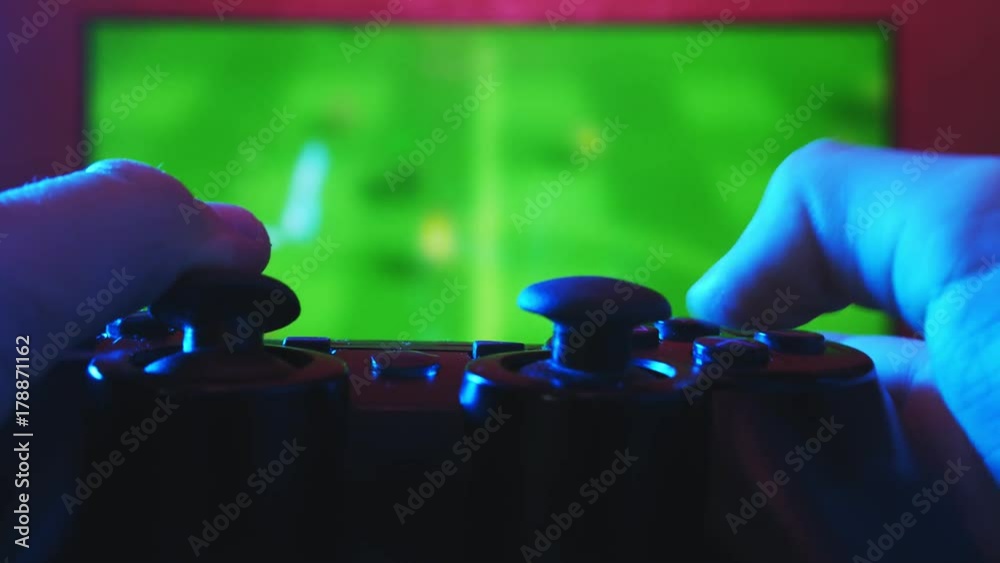 Close view of a gamer's hands playing soccer simulator on his game console using joystick