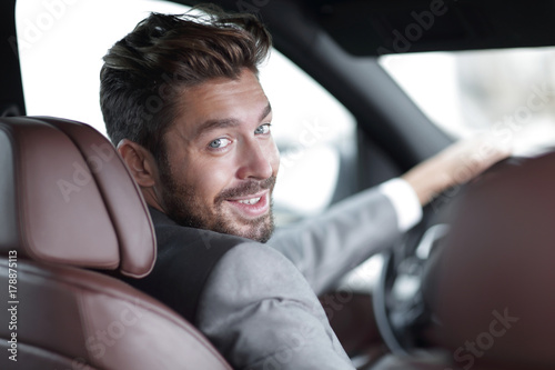 rear view, young man driving his car, looking at camera