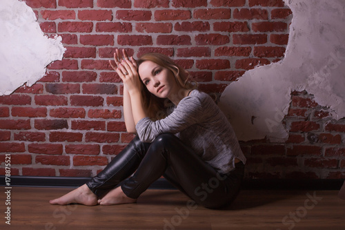 Pretty young model with curly blonde hair, wears casual apparel, posing on a brick wall background