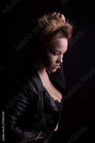 Dramatic portrait of young model with lush wavy hair, wears leather jacket, posing with shadow on her face