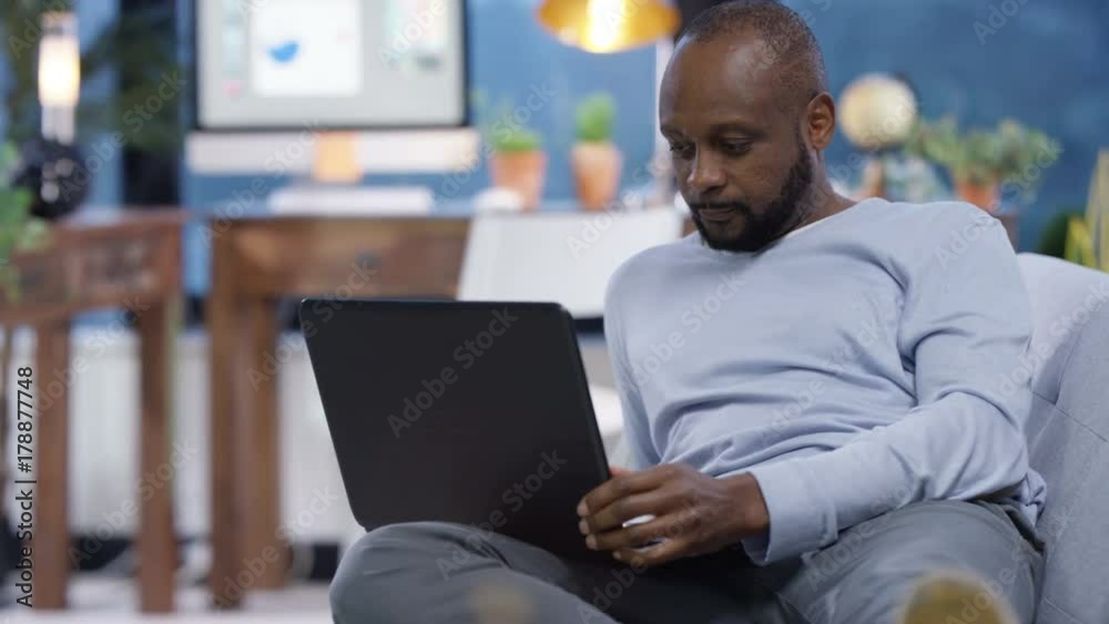  Cheerful casual man relaxing at home, using laptop