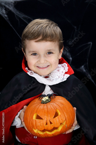 littlechild with vampire costume holding a pumpkin in a black background with spider web photo