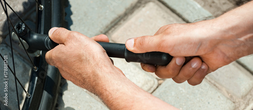The panorama of man pumping bicycle tyre outdoors, close-up of hands.