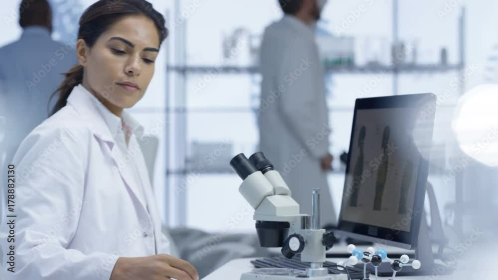 Medical researcher looking at a slide under microscope & working on computer Medical researcher looking at a slide under microscope & working on computer