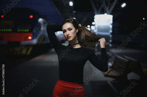 Beautiful young elegant woman traveler waiting for train at evening train station