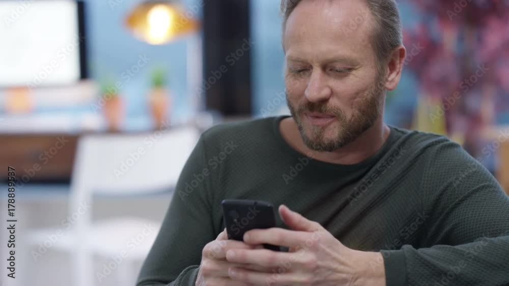 Happy man relaxing at home texting or using internet on his smartphone Happy man relaxing at home texting or using internet on his smartphone