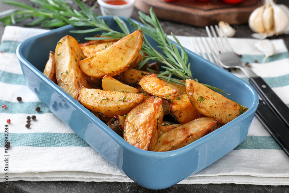 Delicious baked potatoes with rosemary in baking dish on cloth Delicious baked potatoes with rosemary in baking dish on cloth