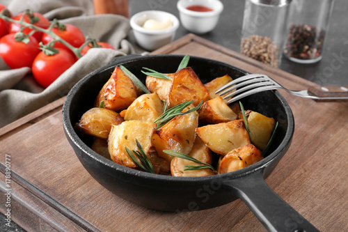 Delicious baked potatoes with rosemary in pan on table
