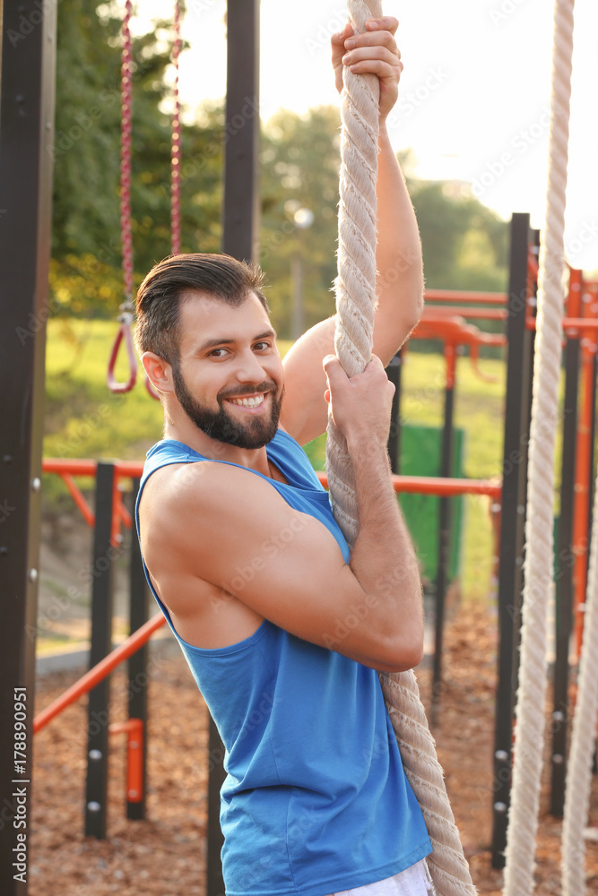 Fototapeta premium Handsome young man doing rope climbing exercise outdoors