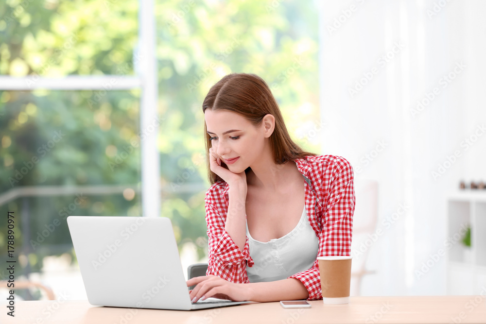 Young lady with modern laptop sitting at table in room Young lady with modern laptop sitting at table in room