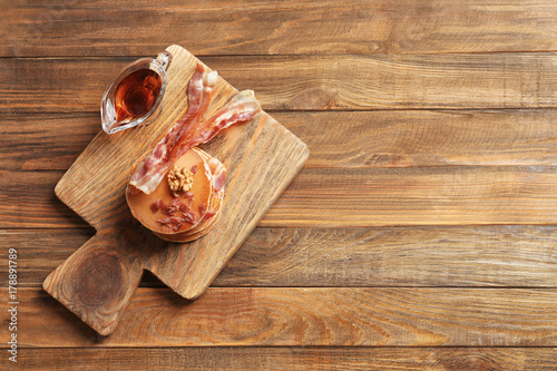 Wooden board with pancakes and bacon on table