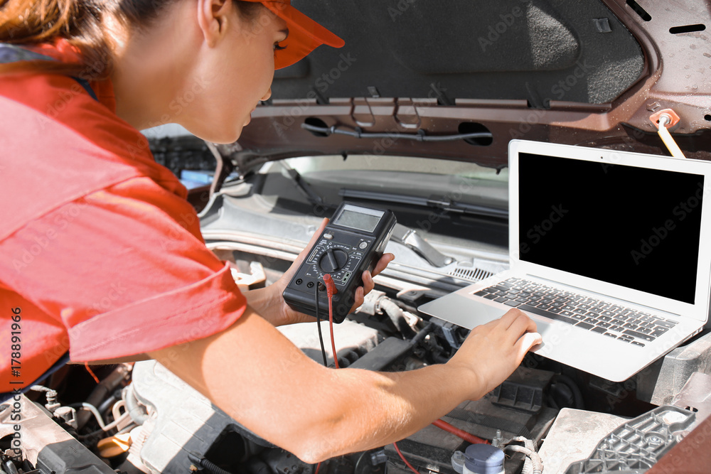 Young female mechanic with laptop repairing car in body shop Young female mechanic with laptop repairing car in body shop