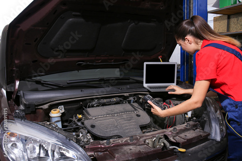 Young female mechanic with laptop repairing car in body shop