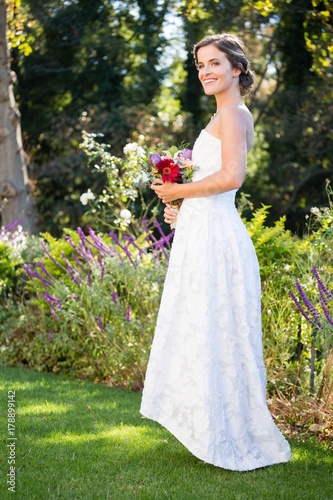 Smiling bride holding bouquet while standing on grassy field