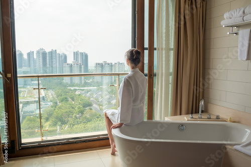Young woman on white bath in luxury bathroom with city view