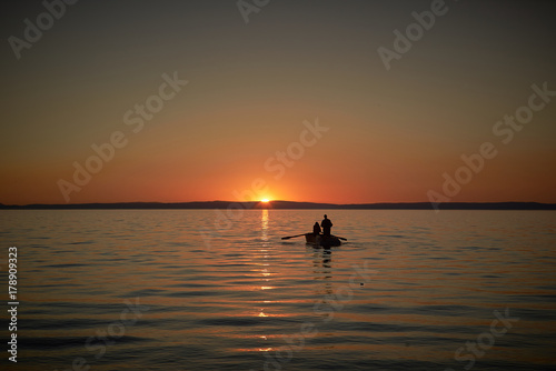 Boat in the sea with two fishermen in it, nets in the sea. Sunset or sunrise