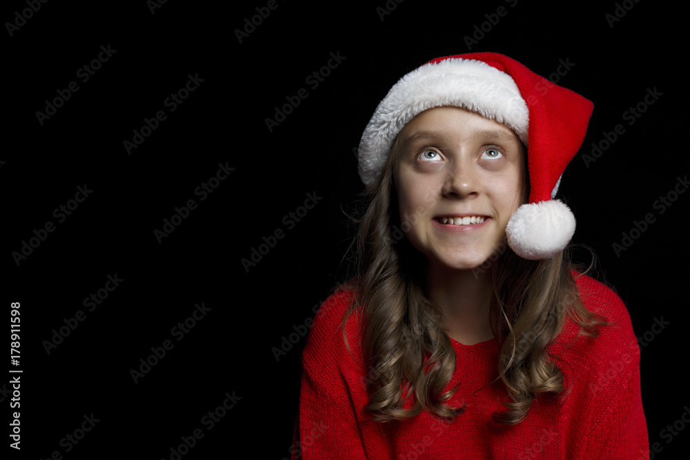 Merry Christmas. A young girl in a red sweater and a Santa Claus hat looks at the viewer. Merry Christmas. A young girl in a red sweater and a Santa Claus hat looks at the viewer.