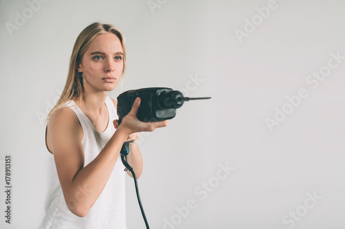 Funny portrait upset craftswoman. Blonde woman is wearing shirt isolated on white. Girl does not know how to use a drill