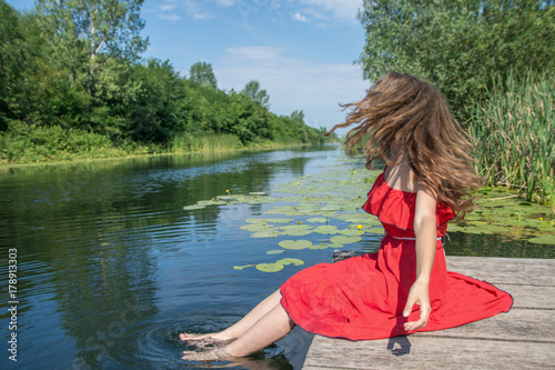 Beautiful young woman in red dress by the river water