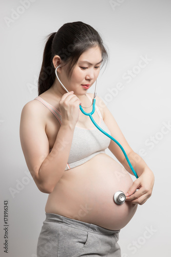 Beautiful pregnant asian woman in grey underwear using stethoscope examining on her baby in her belly.
