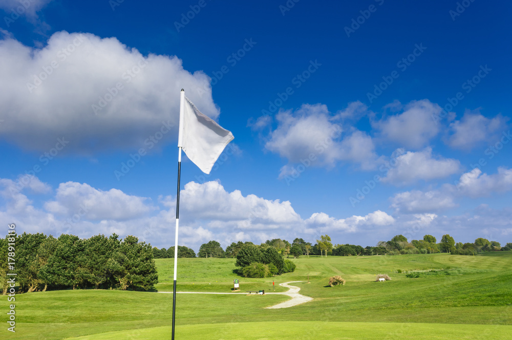 Obraz premium View of a green golf course, hole and flag on a bright sunny day. Sport, relax, recreation and leisure concept. Summer landscape with sunbeams