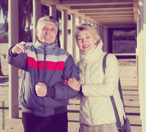 Mature couple walks outdoors and point by hand