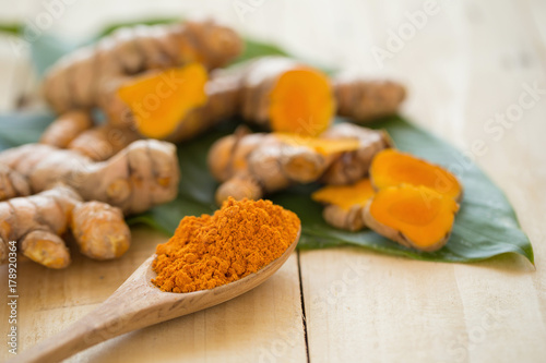 Turmeric powder in a wooden spoon and fresh turmeric on wooden background