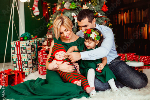 Woman in luxury green dress sits with her husband and two children before a Christmas tree