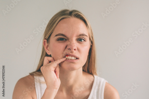 A horizontal photo of a young worried woman in checkered shirt suffering from strong toothache and touching her cheek photo