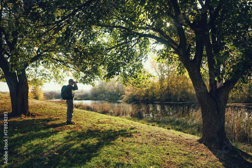 Man is watching birds with binoculars by the river in autumn. photo