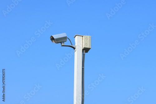 Closed circuit television camera on white steel pole with the background of blue sky.