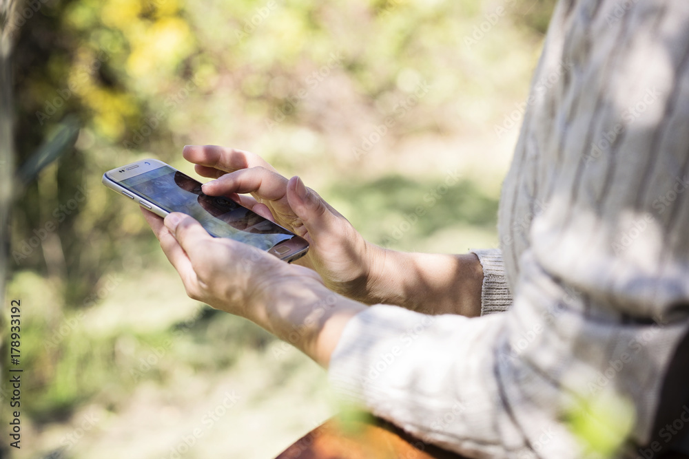 Giovane donna caucasica usa lo smartphone sotto un ulivo in campagna