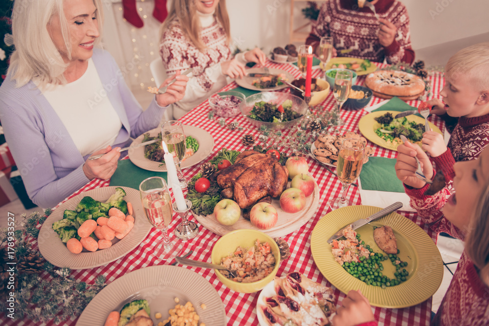 Gathered relatives at nicely served setted desktop with glasses of sparkling wine, in knitted traditional x mas costumes, full of yummy treats, carrots, broccoli, corn, pie, cup-cakes. Bon appetite!