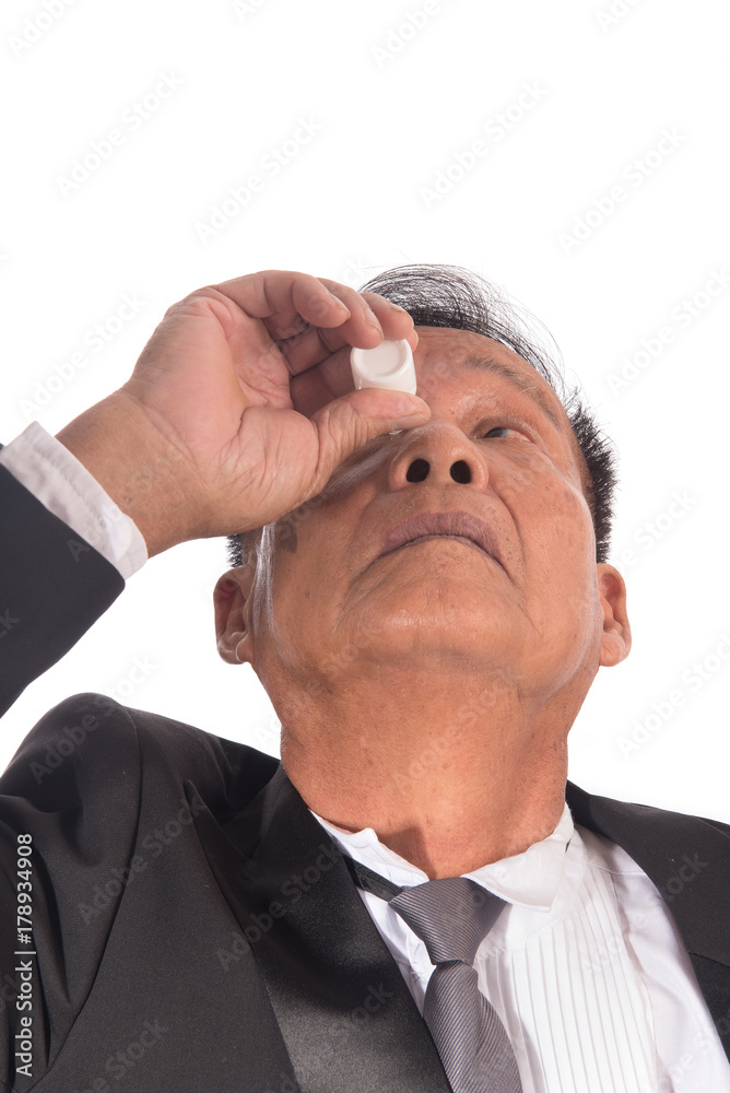 Obraz premium Senior Asian businessman getting the medicine in the eye. Older man applying eye drops isolated on white background. Man has a cataract in his eyes. Health care concept.