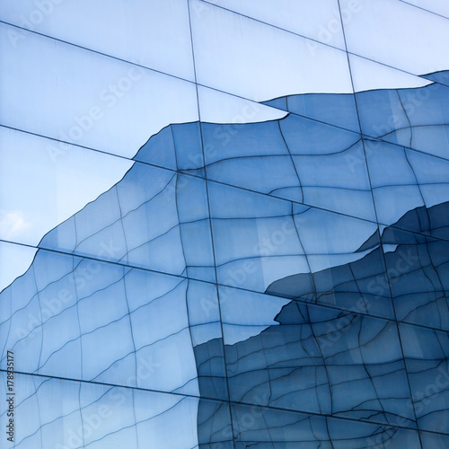 part of geometrically shaped modern glass building with reflections of blue sky and glass wall