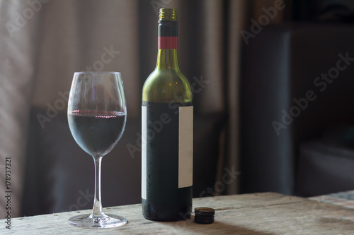 Red wine in glass with bottle on brown wooden table.