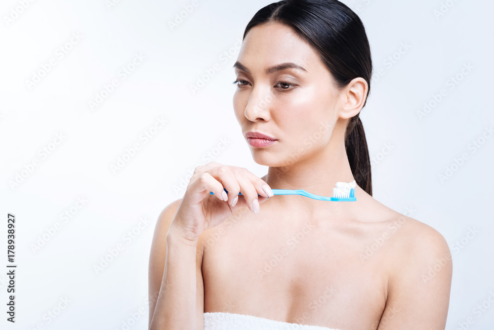 Pleasant woman pondering over something while holding toothbrush