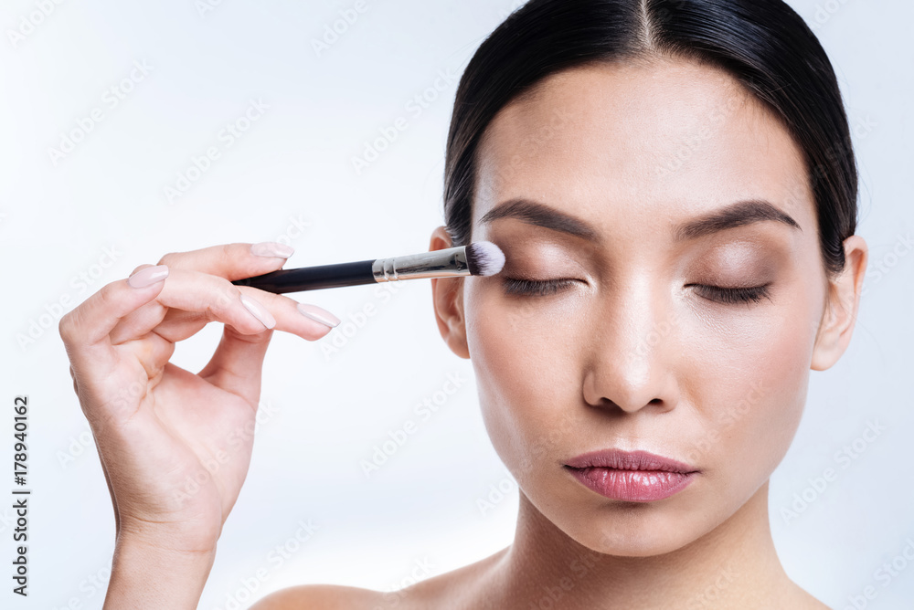 Charming woman applying eye shadows with brush