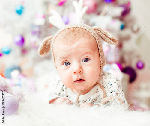 Little boy in a hat with deer ears lies on the floor before a Chirstmas tree