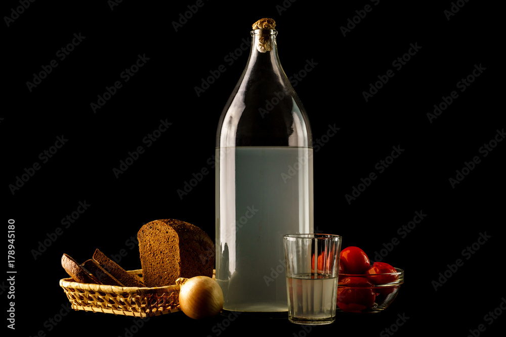 Naklejka premium Ukrainian national drink and snack. The big bottle and glass of moonshine and snack isolated on black background
