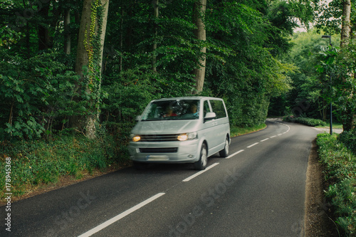 Cars driving on the asphalt road passing through the green forest in the region of Normandy, France. Nature, countryside landscape, transportation and road network concept