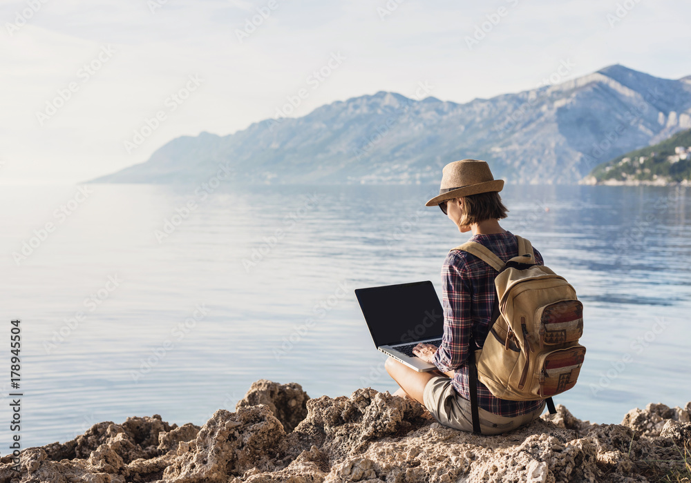 Young woman using laptop computer on a sea. Freelance work concept.People using devices to plan trips, check in to hotels and flights, stay connected to family and office from remote part of the world