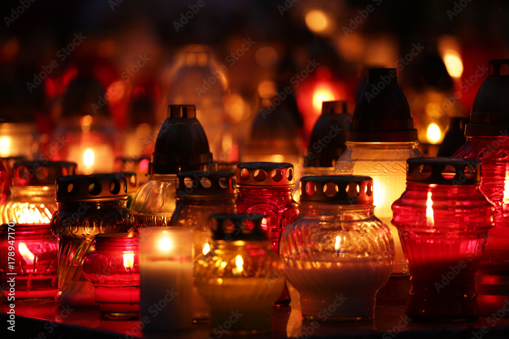 lot of bright, colorful candles standing on graves in the cemetery at night